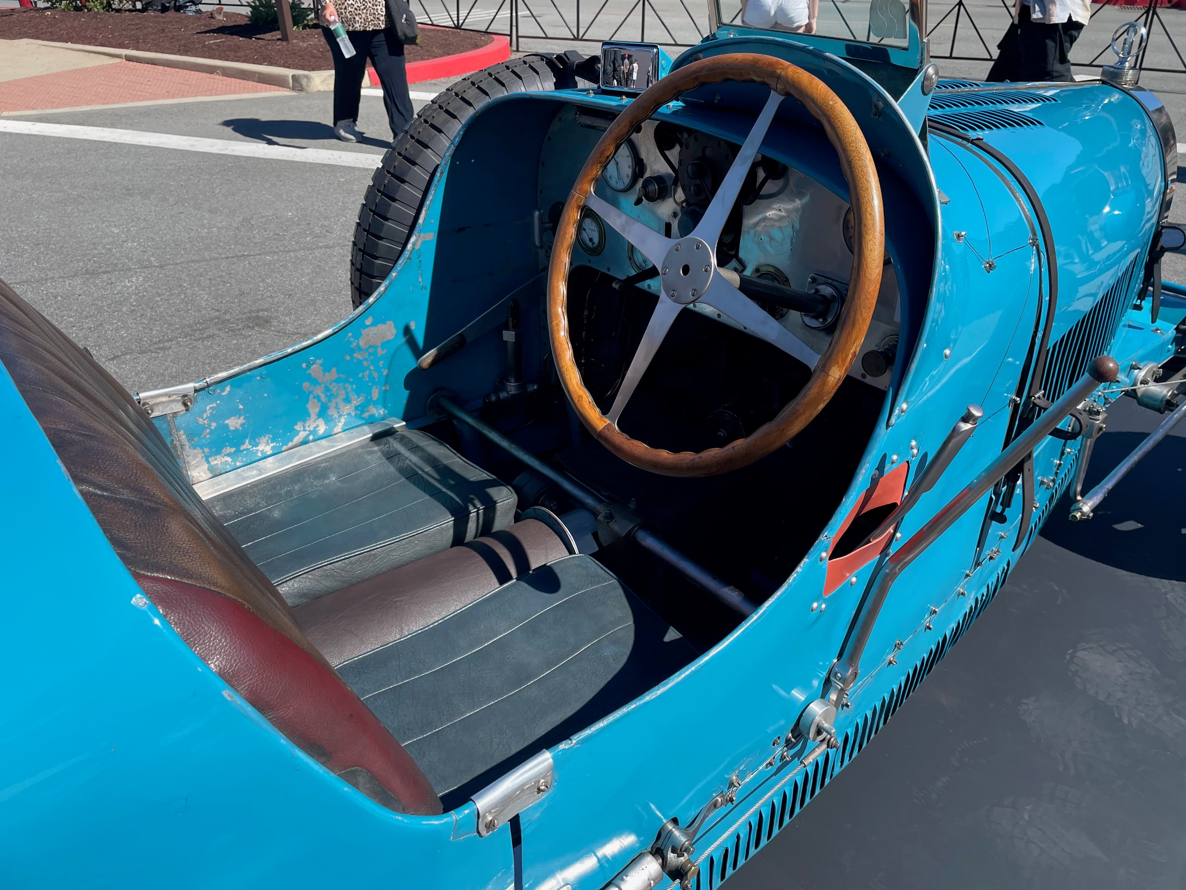 View of the interior of a Bugatti Type 35T from above. Wooden steering wheel, dark gray leather seats, and dashboard with gauges. The exterior has faded French racing blue paint and other signs of age.