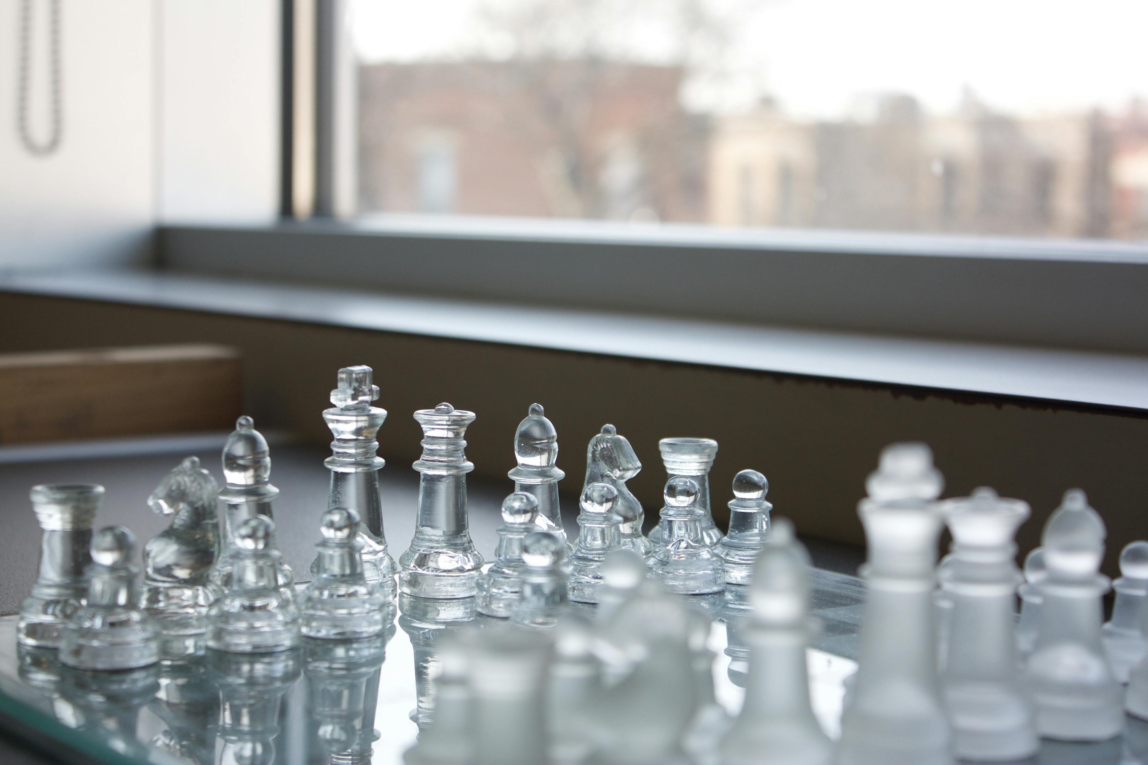 View of a chessboard, angled from above. The blurry outline of a window can be seen in the background.